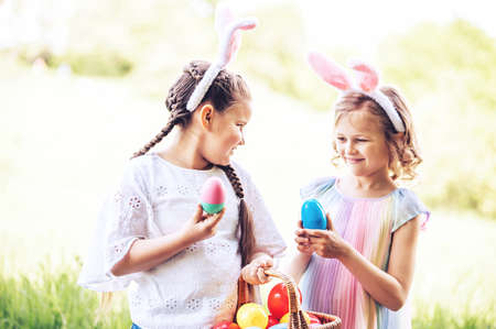 Easter egg hunt. Group Of Children Wearing Bunny Ears Running To Pick Up colorful Egg In Garden. Easter tradition. Laughing children in park with basket spring conceptの写真素材