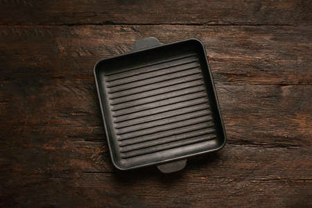 New empty cast-iron grill pan with two handles on wooden background. place for text. Flat lay top view black cast iron skillet for barbecue. Food mockupの写真素材