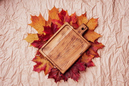 Autumn flat lay composition. Empty wooden plate cutting board and autumn leaves on paper background top view mock up. copy space. Fall season. golden maple leaves.の写真素材