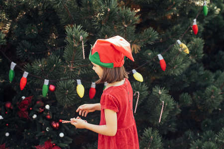 Child waiting for Christmas in wood in summer. portrait of little girl in red dress decorating...