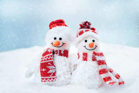 Merry christmas and happy new year greeting card with copy space. Happy two little snowmen in cap and scarf standing in winter snow background. christmas fairytale.の写真素材
