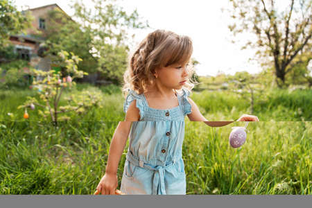 Easter egg hunt. Girl child running to pick up Egg in Garden. Easter tradition. Baby with basket...