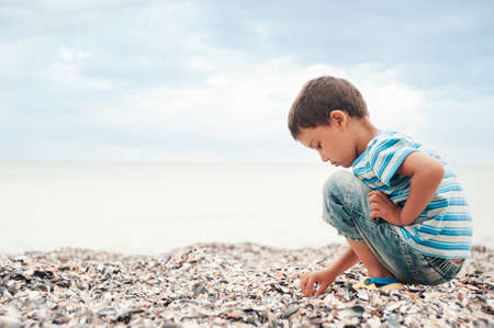 little boy by sea collects seashells on beach. sunset. Happy childhood. summer vacation at sea or ocean.の写真素材