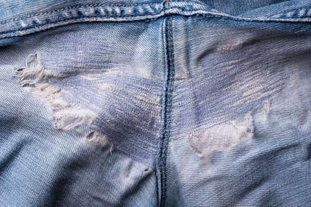 Closeup of torn old blue jeans background. texture of ripped damaged destroyed denim jeans. hole and scuffs on jeans between legs. repair by sewing machine and stitchingの写真素材