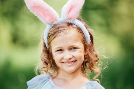 Cute funny girl with Easter eggs and bunny ears at garden. easter concept. Laughing child at Easter egg hunt. Child in park with basket full of eggs, spring conceptの写真素材
