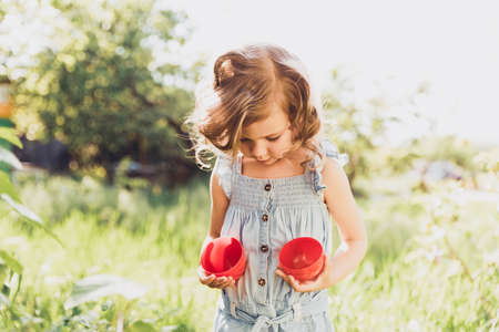 Easter egg hunt. Girl child Wearing Bunny Ears Running To Pick Up Egg In Garden. Easter tradition. Baby with basket full of colorful eggs.の写真素材