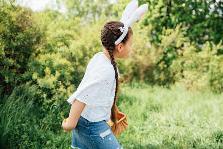 Easter egg hunt. Girl child Wearing Bunny Ears Running To Pick Up Egg In Garden. Easter tradition....