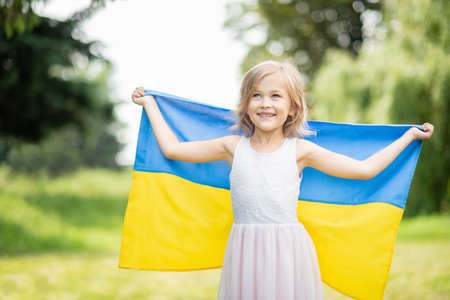 Child carries fluttering blue and yellow flag of Ukraine in field. Ukraines Independence Day. Flag Day. Constitution day. Girl in traditional embroidery with flag of Ukraineの写真素材