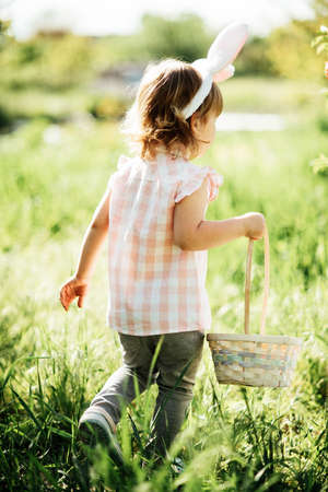 Easter egg hunt. Girl child Wearing Bunny Ears Running To Pick Up Egg In Garden. Easter tradition....