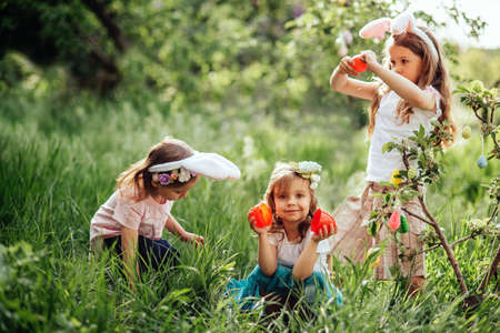 Easter egg hunt. Group Of Children Wearing Bunny Ears Running To Pick Up colorful Egg On Easter Egg Hunt In Garden. Easter tradition. Laughing children in park with basket spring conceptの写真素材