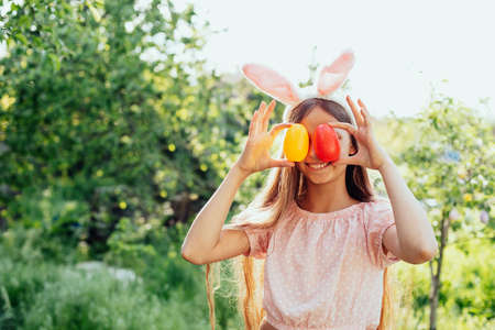 Cute funny girl with Easter eggs and bunny ears at garden. easter concept. Laughing child at Easter...