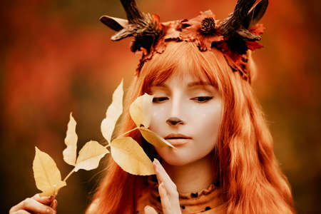 fairy woman with deer horns in autumn forest. Face painting. Beautiful mystery woman. redhead girl with big eyes magical sightの写真素材