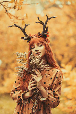 fairy woman with deer horns in autumn forest. Face painting. Beautiful mystery woman. redhead girl with big eyes magical sightの写真素材