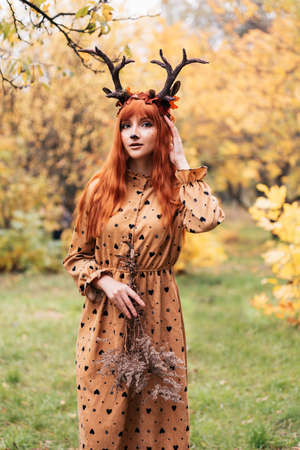 fairy woman with deer horns in autumn forest. Face painting. Beautiful mystery woman. redhead girl with big eyes magical sightの写真素材