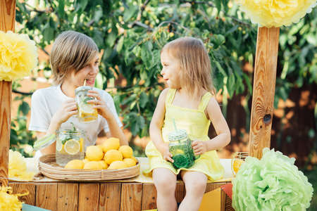 Children drinking natural lemonade at stand in park. Summer refreshing natural drink lemonade. Detox fruit infused flavored water, cocktail in a beverage dispenser with fresh fruitsの写真素材
