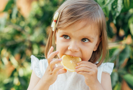 Cute little Child girl eating fresh lemon in nature in countryside. Healthy lifestyle and clean eating concept. Fruits and vegetables. natural vitamins - fresh lemonsの写真素材