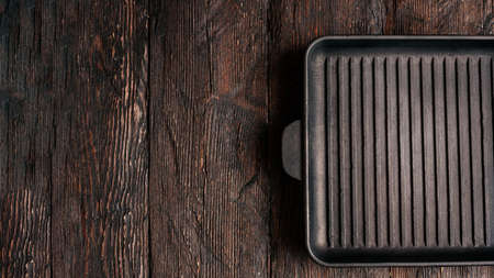 New empty cast-iron grill pan with two handles on wooden background. place for text. Flat lay top view black cast iron skillet for barbecue. Food Mockupの写真素材