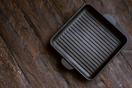 New empty cast-iron grill pan with two handles on wooden background. place for text. Flat lay top view black cast iron skillet for barbecue. Food Mockupの写真素材