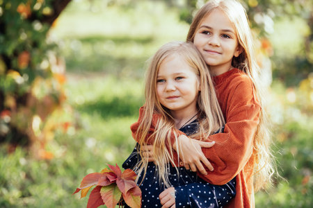 portrait of two happy sisters laughing hugging each other on warm and sunny summer day in garden. people, emotions and friendship concept. Having fun together, positive emotions, bright colors.の写真素材