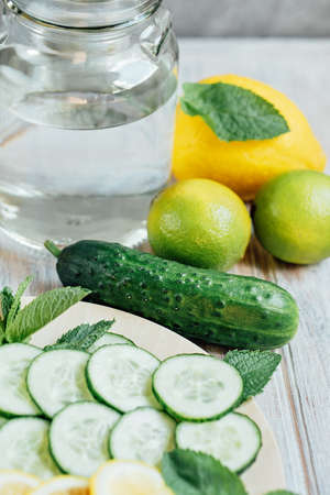 Sassi water, cooking ingredients for making sassi drink: lemon, cucumbers, ginger root, mint on a round wooden tray. Light background. Close-upの写真素材