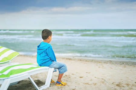 Sad alone kid sitting on beach, looking at sea and thinking. The end of summer. sadness about end of vacationの写真素材