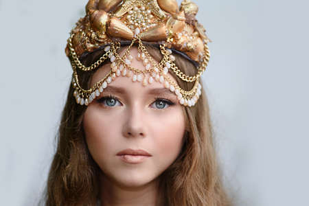 Fantasy woman real mermaid with trident myth goddess of sea with golden tail sitting in sunset on rocks.. Gold hair crown shells pearls jewelry. Mermaid sitting on shore. fantasy concept.の写真素材