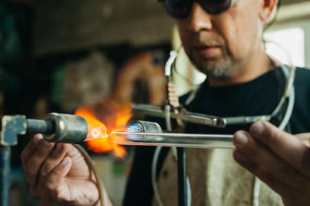 Close up of glass blower working with flame. Concept of handmade, high quality, artisan. Production of neon tubes. gas burner. detail of craft and craftsmanship. melt blownの写真素材