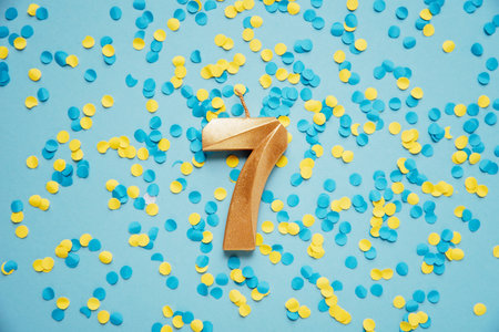 Number 7 seven golden celebration birthday candle on yellow and blue confetti Background. seven years birthday. concept of celebrating birthday, anniversary, important date, holidayの写真素材