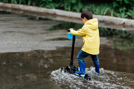 Little boy in raincoat and rubber boots playing in puddle. Fun on street. body hardening in summer....