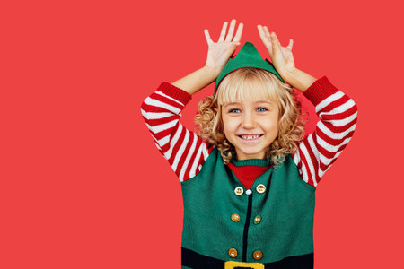 Merry Christmas Little girl in Santa elf helper costume on bright red vivid color background. Red...