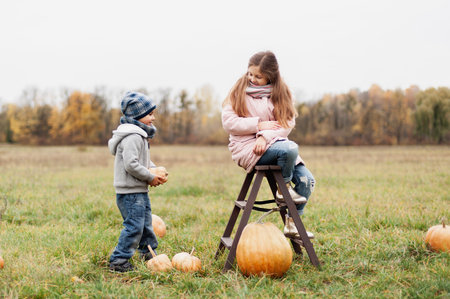 Autumn harvest organic pumpkins and apples. Happy children on pumpkin patch on cold autumn day, with lot of pumpkins for halloween or thanksgiving and red wagon. Boy and girl on pumpkin field.の写真素材