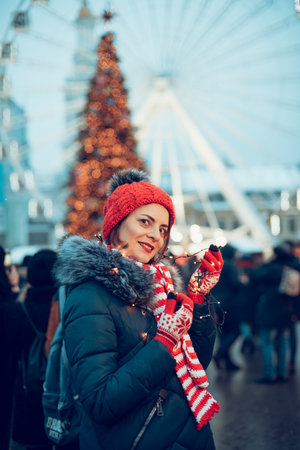 cute lovely woman in warm clothes on christmas market outdoors in winter snow day. Christmas Big Ferris Wheel lights. holidays, winter and people concept.の写真素材