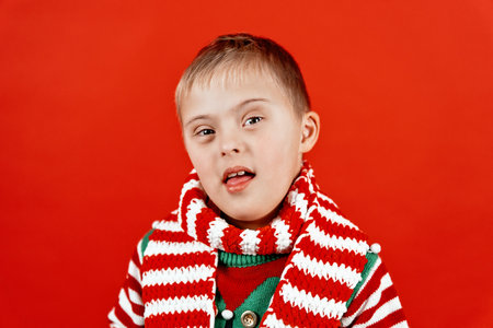 Happy child with Down syndrome in Christmas scarf having fun and laughing in studio. Christmas mood. happy new year. Portrait on red backgroundの写真素材