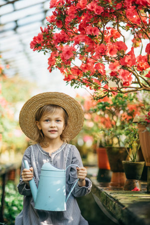 Child planting spring flowers. Little girl gardener plants azalea. Girl holding azalea bush in flower pot. Child taking care of plants. Toddler with flower basket. girl holding pink flowersの写真素材