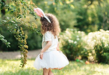 Easter egg hunt. Girl child Wearing Bunny Ears Running To Pick Up Egg In Garden. Easter tradition....