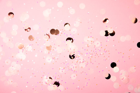 Abstract background of scattered pink and gold confetti with bokeh lights, creating a festive and...
