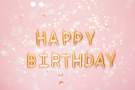 Golden Happy Birthday letter candles arranged on a pink background with scattered confetti, creating a festive and cheerful celebration scene. celebrating birthday with touch of elegance and charmの写真素材