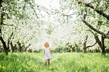 girl sniffing flowers of apple orchard. garden with flowering trees. Allergy season. Soft focus. Girl enjoying floral aroma. Child enjoy life without allergy.の写真素材