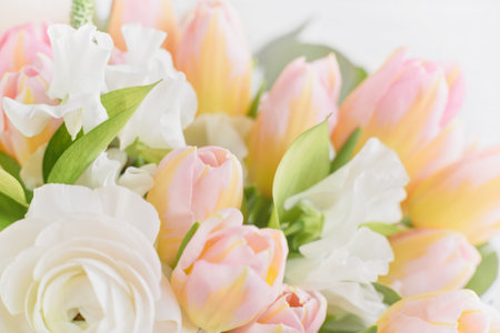 Beautiful holiday card. Mother Day greeting card. Delicate bouquet of white ranunculus and pastel tulips with soft green leaves, creating a romantic and elegant floral sceneの写真素材