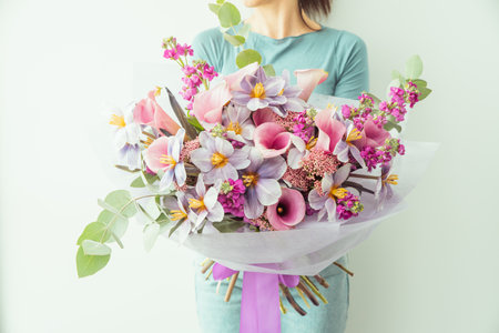 Woman holding large bouquet of flowers wrapped in purple paper. bouquet in shades of pink, purple and white lilies, tulips and other small flowers. floral card. Mothers day, International Womens Dayの写真素材