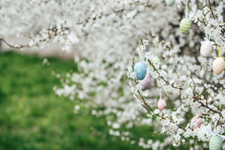 Easter Greeting Card. Easter eggs hanging on blossoming tree branches with white spring flowers and...