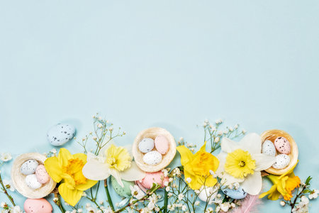 Flat lay of Easter eggs, decorative nests, and blue feathers on pastel blue background, greeting...