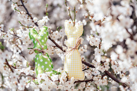 Colorful fabric Easter bunnies placed on blooming cherry tree branches with white flowers creating a...