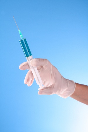 Syringe in doctors hand over blue backgroundの写真素材