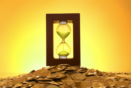 Hourglass and coins on yellow background