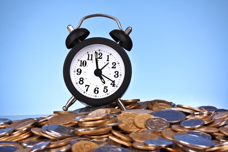 Alarm clock with golden coins on blue background. Ukrainian coins