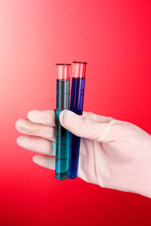 Test tubes with fluid in hand on red backgroundの写真素材