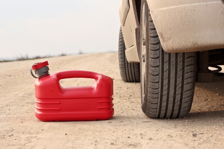 Red plastic fuel canister on dirt road with carの写真素材