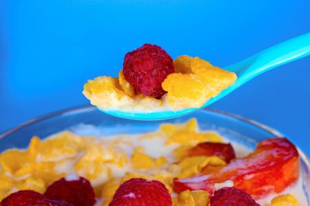 tasty cornflakes, fruit and milk in glass bowl on blue backgroundの写真素材