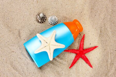 sunblock in bottle, shells and starfish on sand